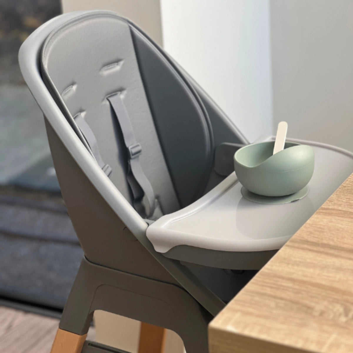 MOOSE Harper High Chair with padded seat, safety harness and feeding tray beside a dining table.