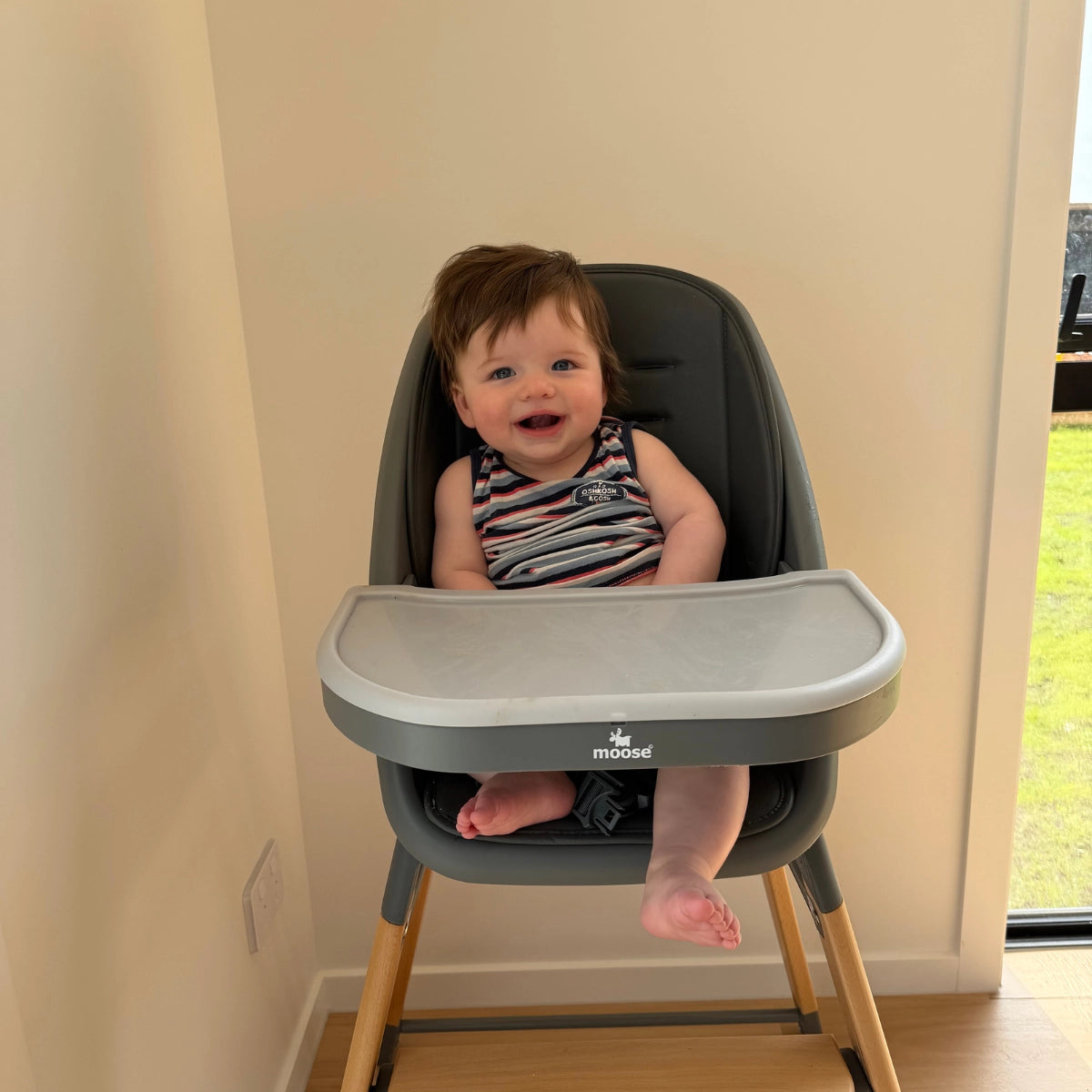 Toddler sitting in the charcoal grey MOOSE Harper High Chair with natural wooden legs.