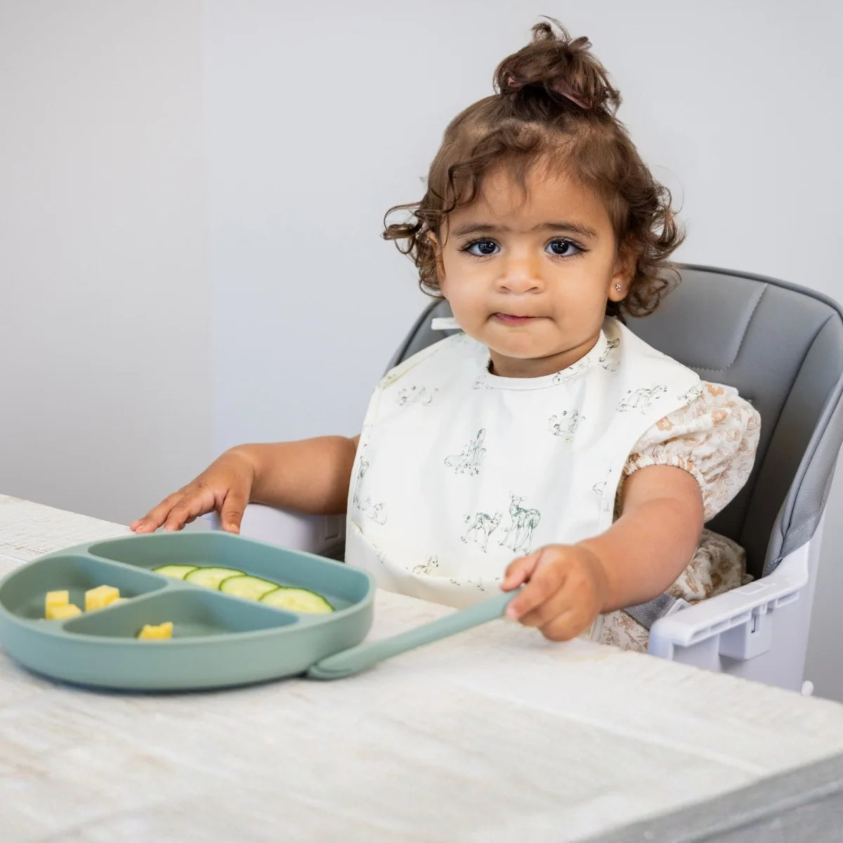 Toddler eating from a divided plate in the MOOSE Frankie high chair with the feeding tray attached.
