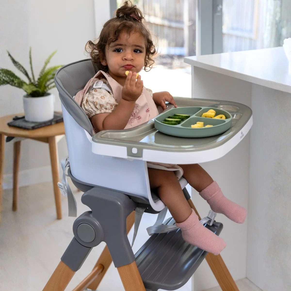 Toddler seated in the MOOSE Frankie high chair with a divided plate of food on the feeding tray.
