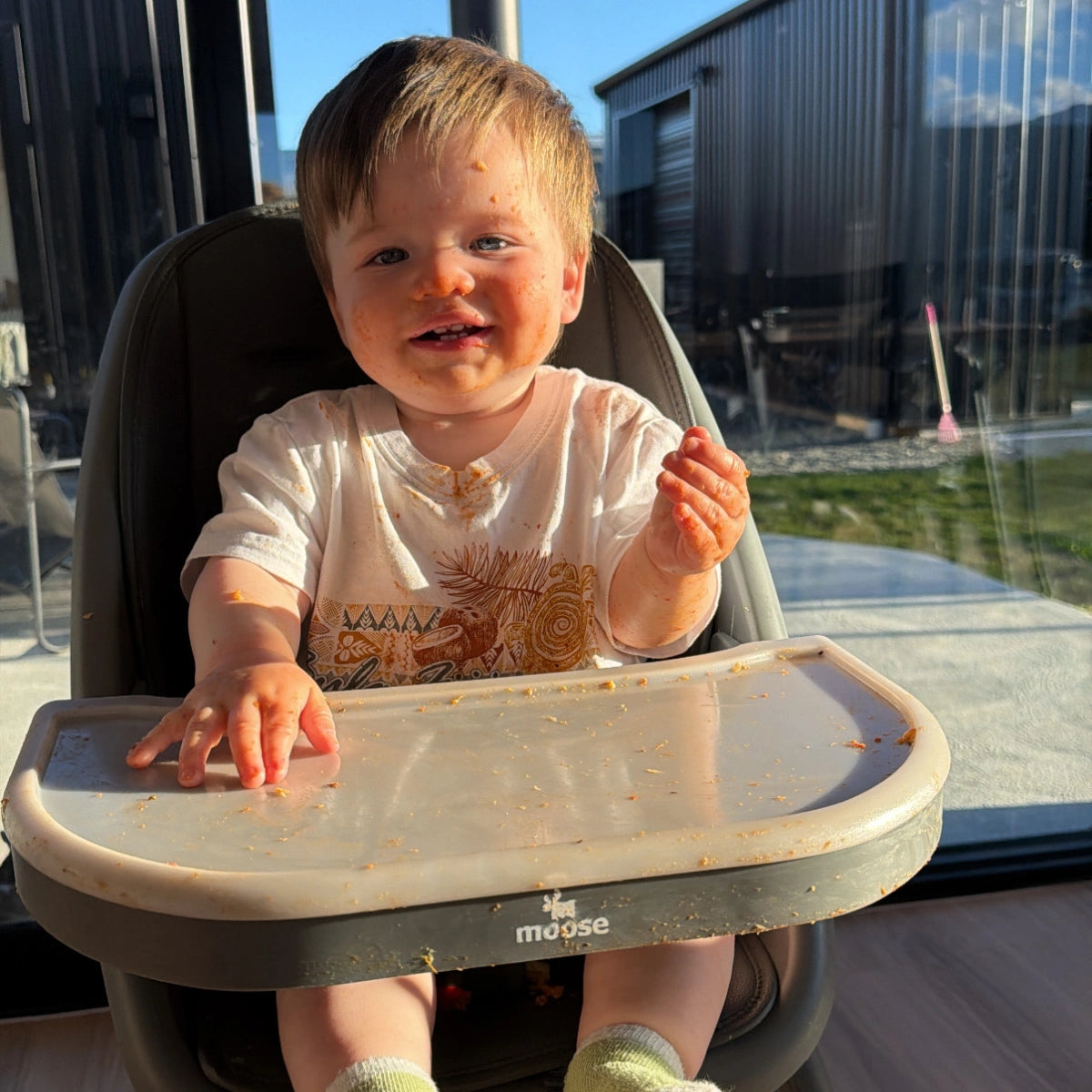 Baby sitting in the MOOSE Harper High Chair with a feeding tray during mealtime.
