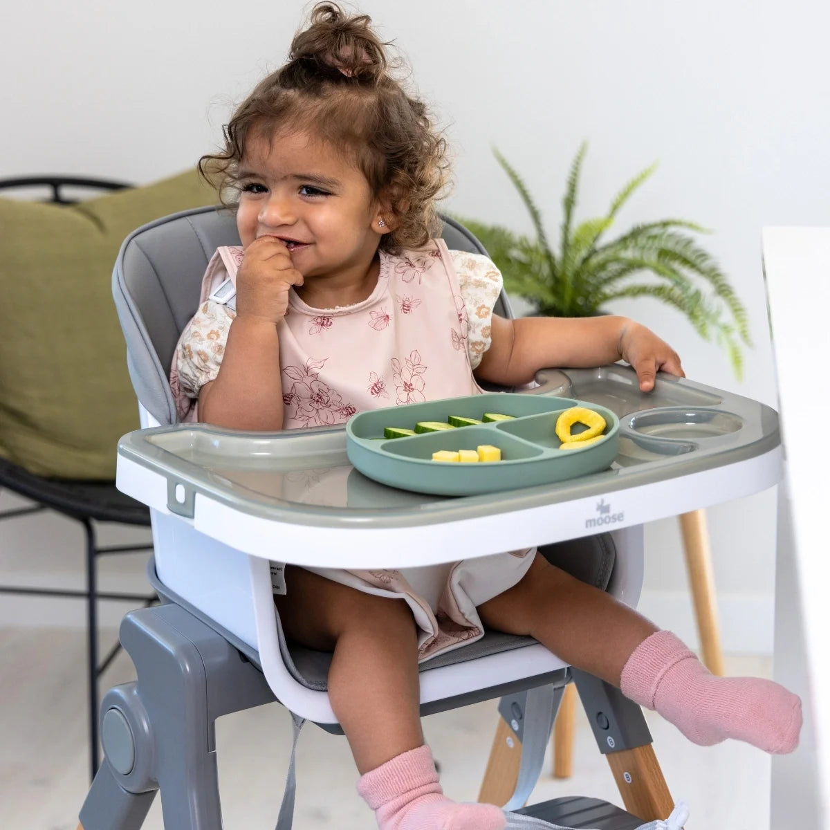 Toddler feeding themselves in the MOOSE Frankie high chair with food on the tray.