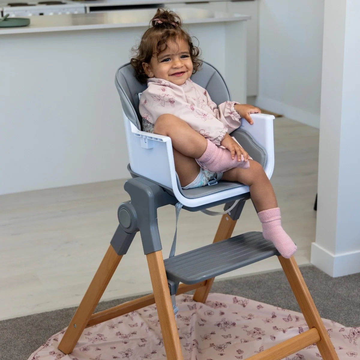 Side view of a toddler sitting in the MOOSE Frankie high chair with wooden legs and footrest visible.