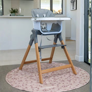 MOOSE Frankie Foldable High Chair in grey with feeding tray, natural wooden legs and footrest, standing on a round rug.