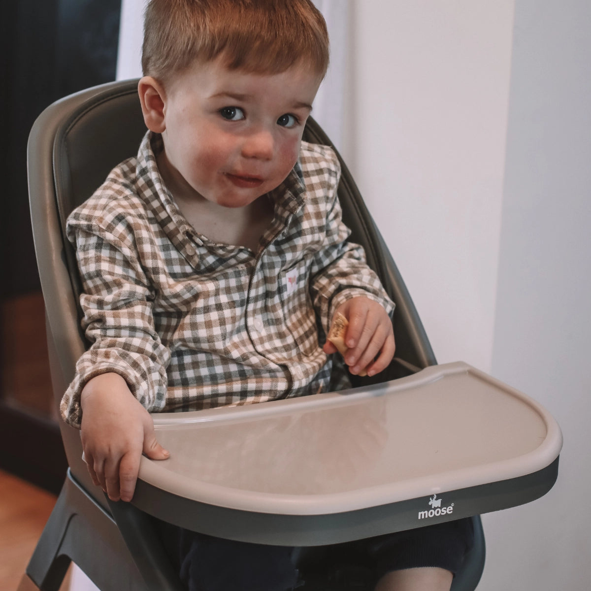 Toddler sitting in the charcoal grey MOOSE Harper High Chair with the feeding tray attached.