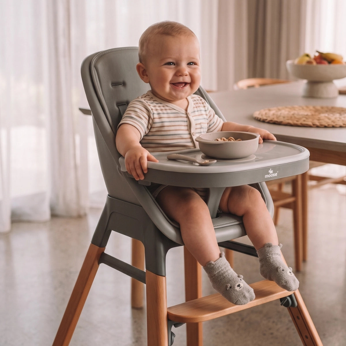 Baby seated in the MOOSE Harper High Chair at a dining table, with feeding tray and wooden footrest.