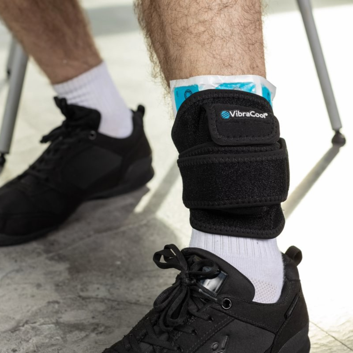 A VibraCool Extended ankle wrap being worn around a person's ankle, shown in a real-world setting with black sneakers and white socks.