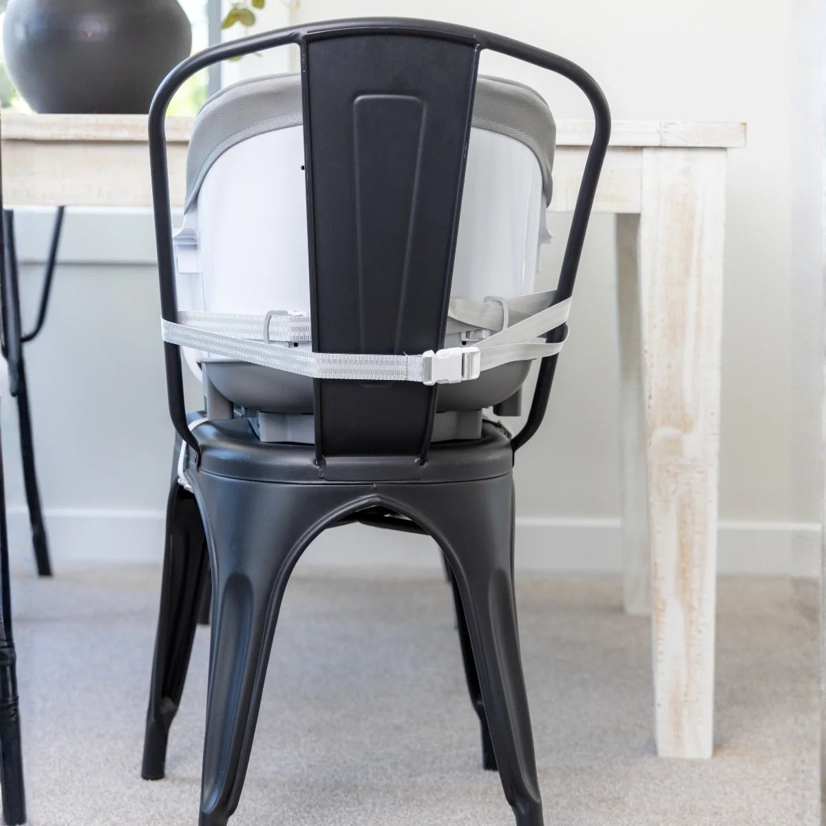 Rear view of the MOOSE Frankie booster seat strapped to a dining chair beside a table.