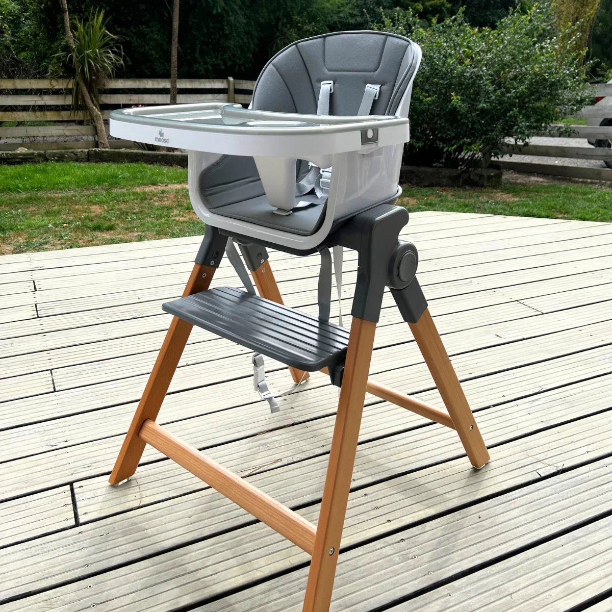 MOOSE Frankie Foldable High Chair on a wooden deck, showing the grey seat, feeding tray and natural wooden legs.